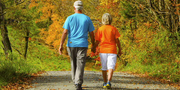 An elderly couple strolling along a path surrounded by autumn foliage.