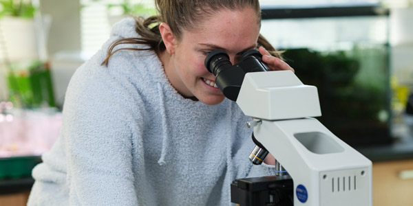 A female scientist in a lab coat examining a specimen under a microscope.